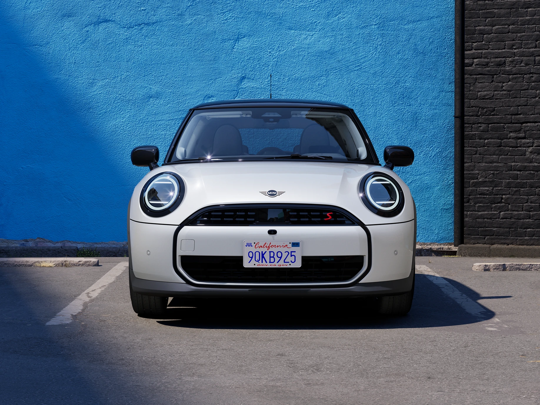 Priekšējais skats uz MINI Cooper Nanuq baltā krāsā ar melnu jumtu, kas novietots stāvvietā.