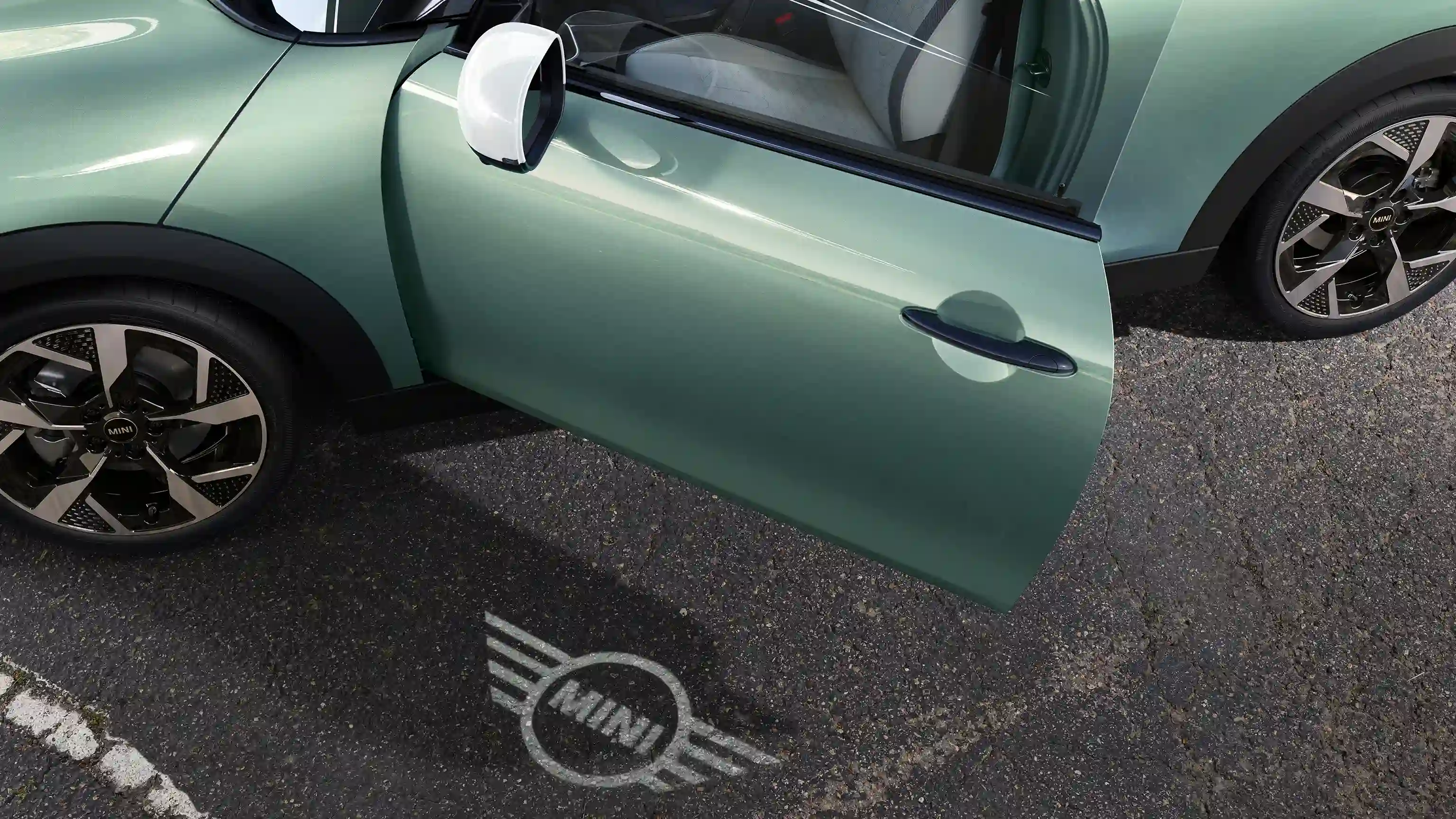 MINI Cooper eksterjera skats ar atvērtām durvīm un MINI logo apsveikuma gaismu uz zemes