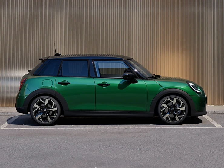 Skats no sāniem uz stāvvietā novietotu piecdurvju MINI Cooper British Racing Green krāsā un jumtu Black krāsā.