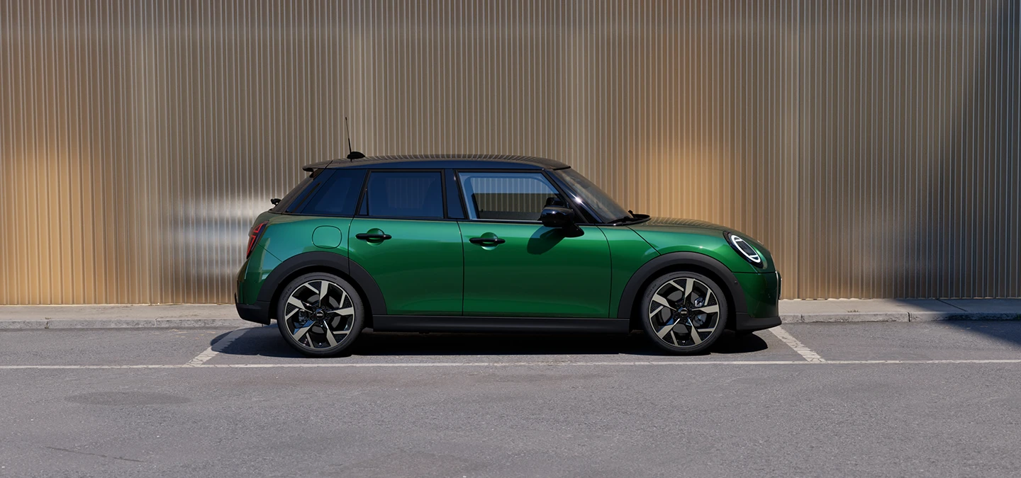 Skats no sāniem uz stāvvietā novietotu piecdurvju MINI Cooper British Racing Green krāsā un jumtu Black krāsā.