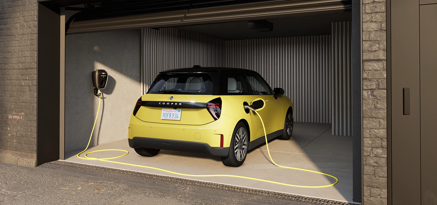 Pilnībā elektriskais MINI Cooper Sunnyside Yellow krāsā, veicot uzlādi garāžā, aizmugures skats.