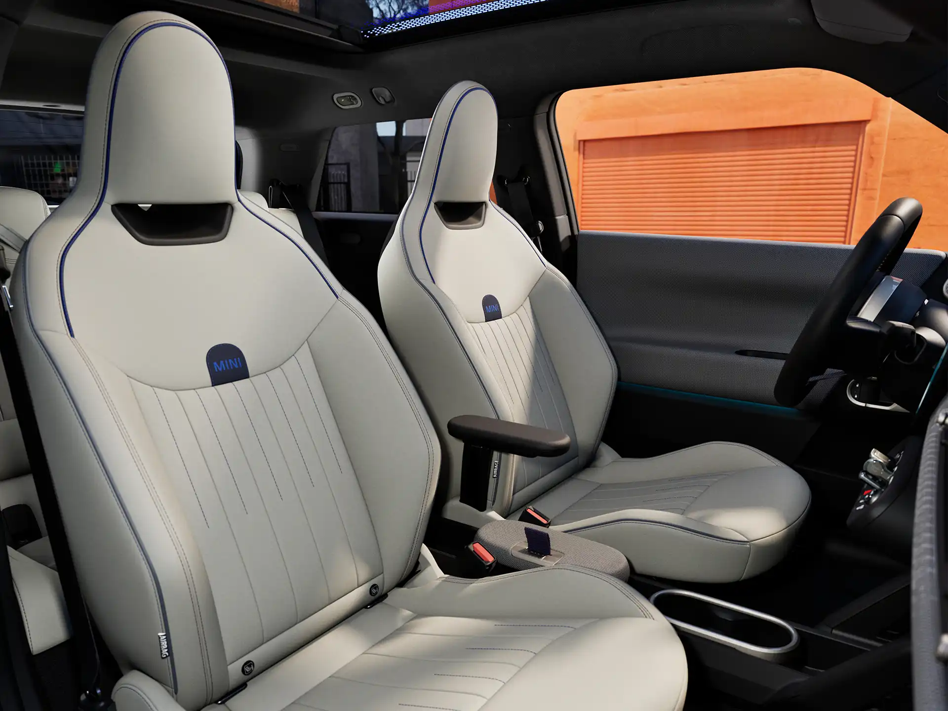 Pilnībā elektriskā MINI Cooper salona perspektīvā redzams instrumentu panelis, stūre, apaļais displejs, panorāmas jumts un priekšējo sēdekļu aizmugure