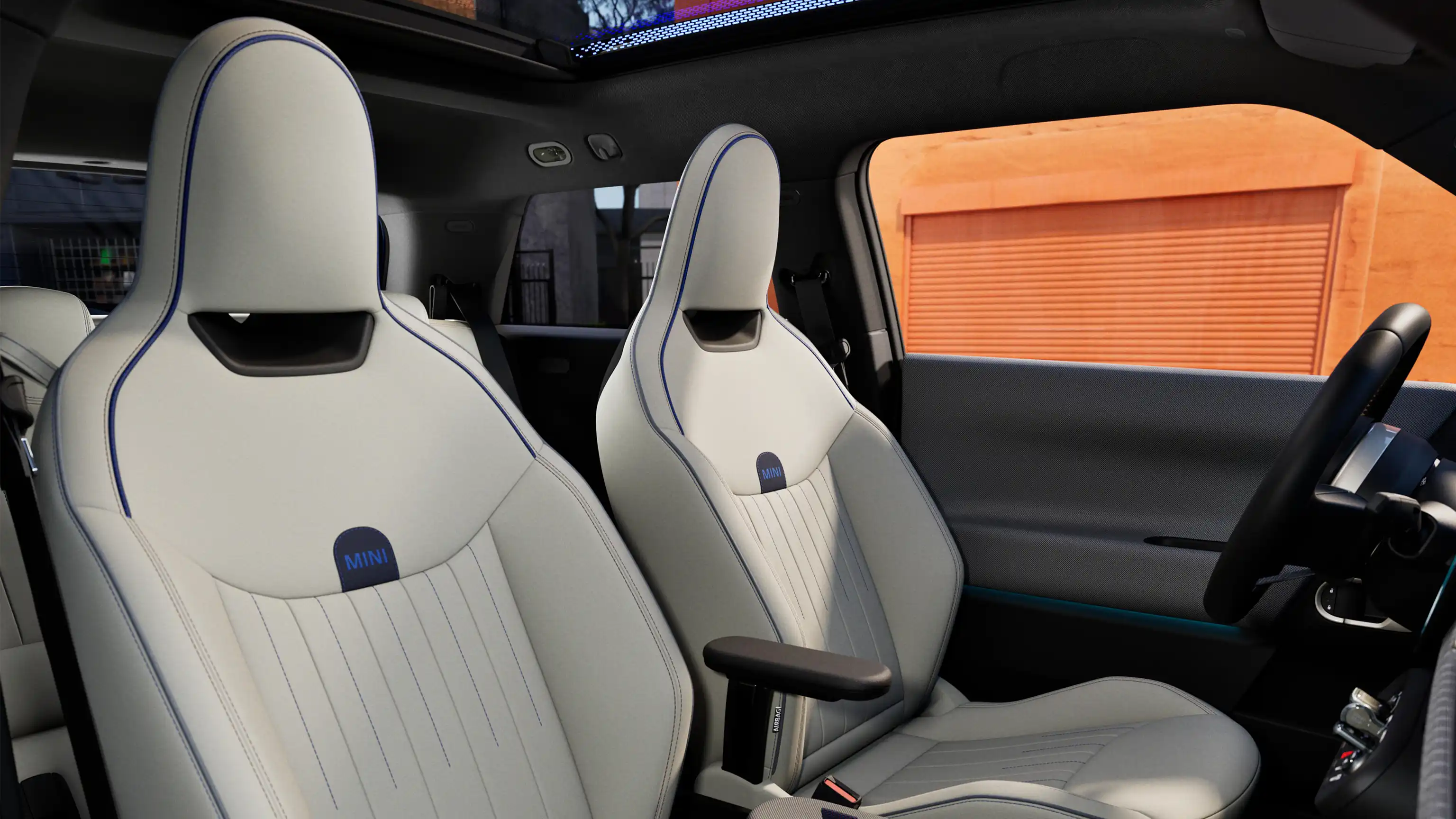 Pilnībā elektriskā MINI Cooper salona perspektīvā redzams instrumentu panelis, stūre, apaļais displejs, panorāmas jumts un priekšējo sēdekļu aizmugure