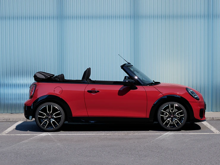 Sānskats uz MINI Cooper Convertible Chili Red krāsā, kas atrodas uz ielas.