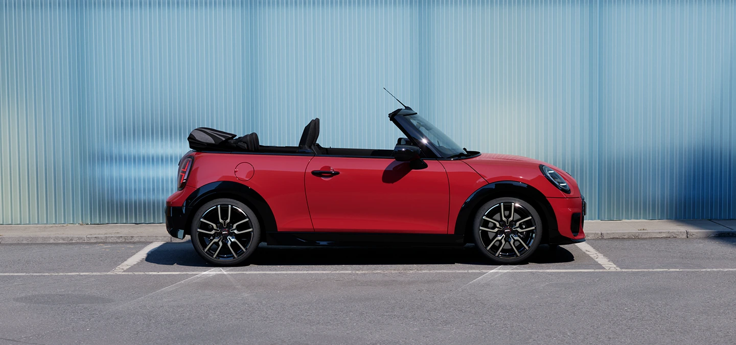 Sānskats uz MINI Cooper Convertible Chili Red krāsā, kas atrodas uz ielas.