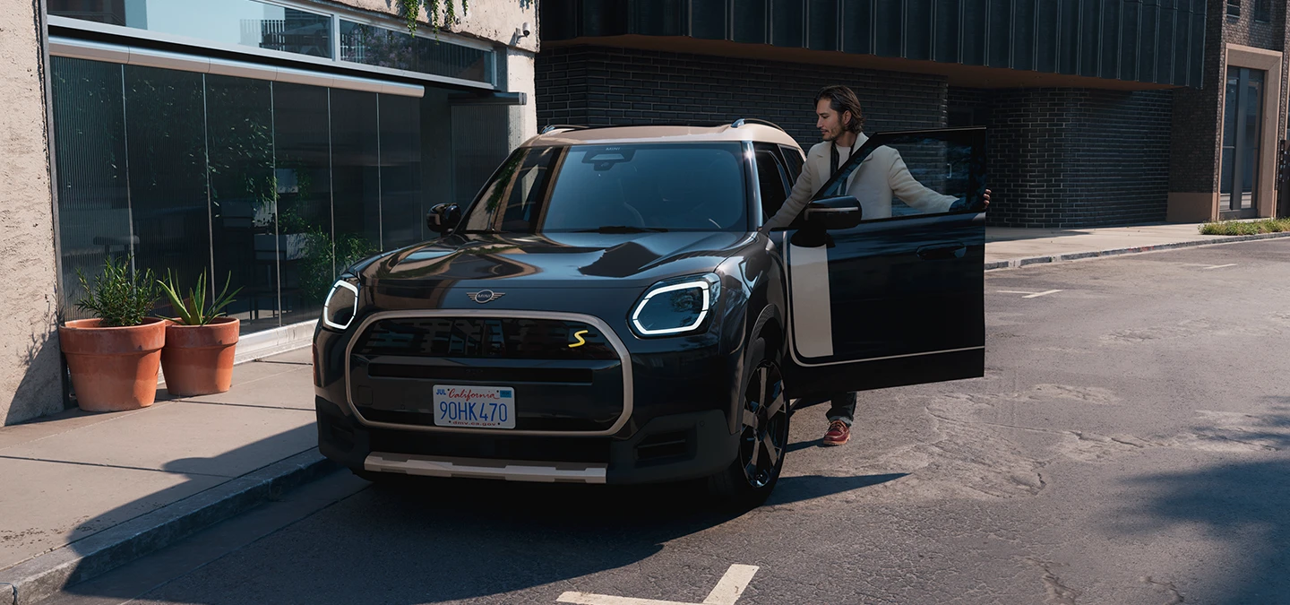 Pilnībā elektriskā MINI Countryman Midnight Black krāsā ar Vibrant Silver krāsas jumtu, priekšskats uz ielas.