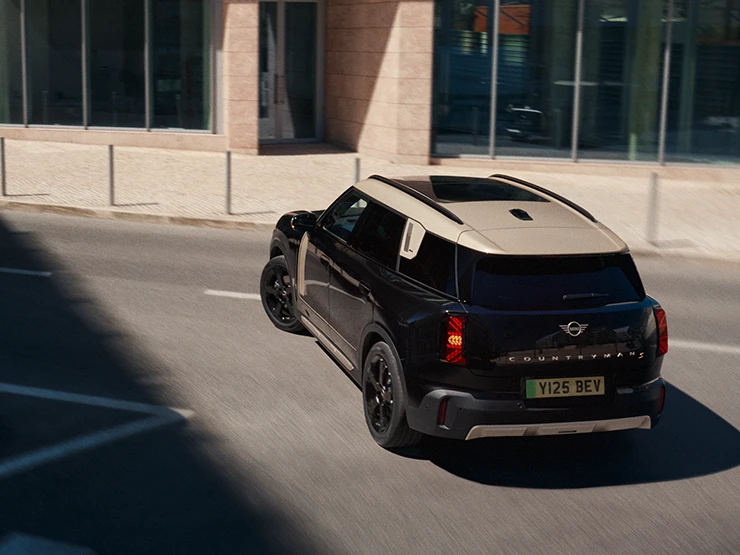 Aizmugures skats no augšas uz stāvvietā novietotu pilnībā elektrisko MINI Countryman Midnight Black krāsā ar Vibrant Silver krāsas jumtu.