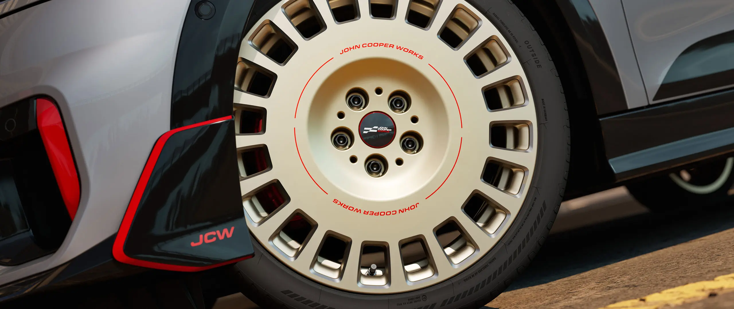 Priekšējā apakšējā spoilera un 18 collu JCW Rallye Spoke 964 diska divtoņu Vibrant Silver krāsā ar dimanta frēzējumiem detalizēts tuvplāns.