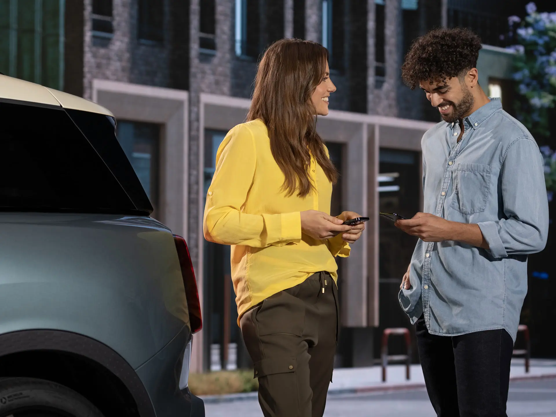 Vīrietis un sieviete stāv pie MINI automobiļa un izmanto savus telefonus, lai sazinātos ar MINI servisa partneri.